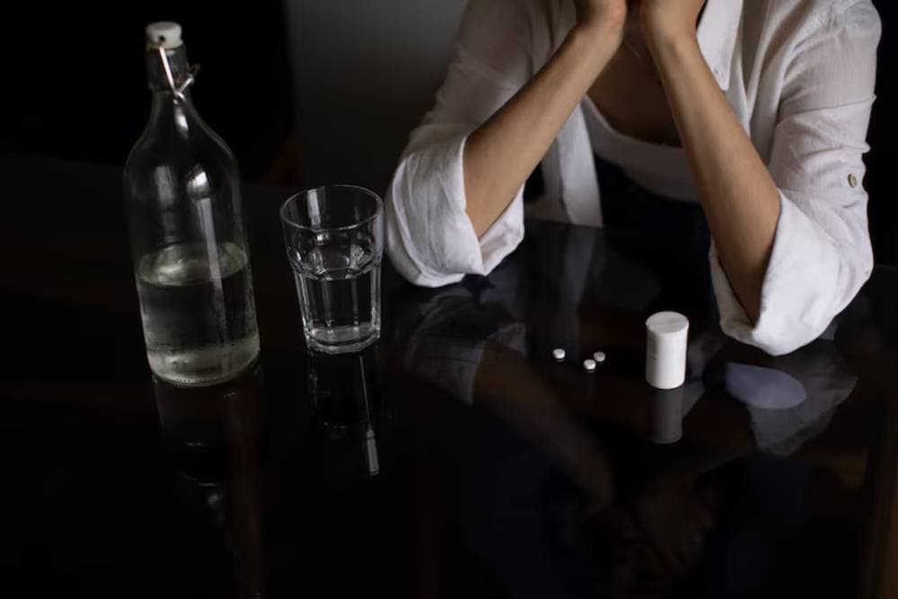 Person sitting at a table with pills and a glass of water, symbolizing the struggle with addiction and the need for Drug Rehab in Orange County. Person sitting at a table with pills and a glass of water, symbolizing the struggle with addiction and the need for Drug Rehab in Orange County.