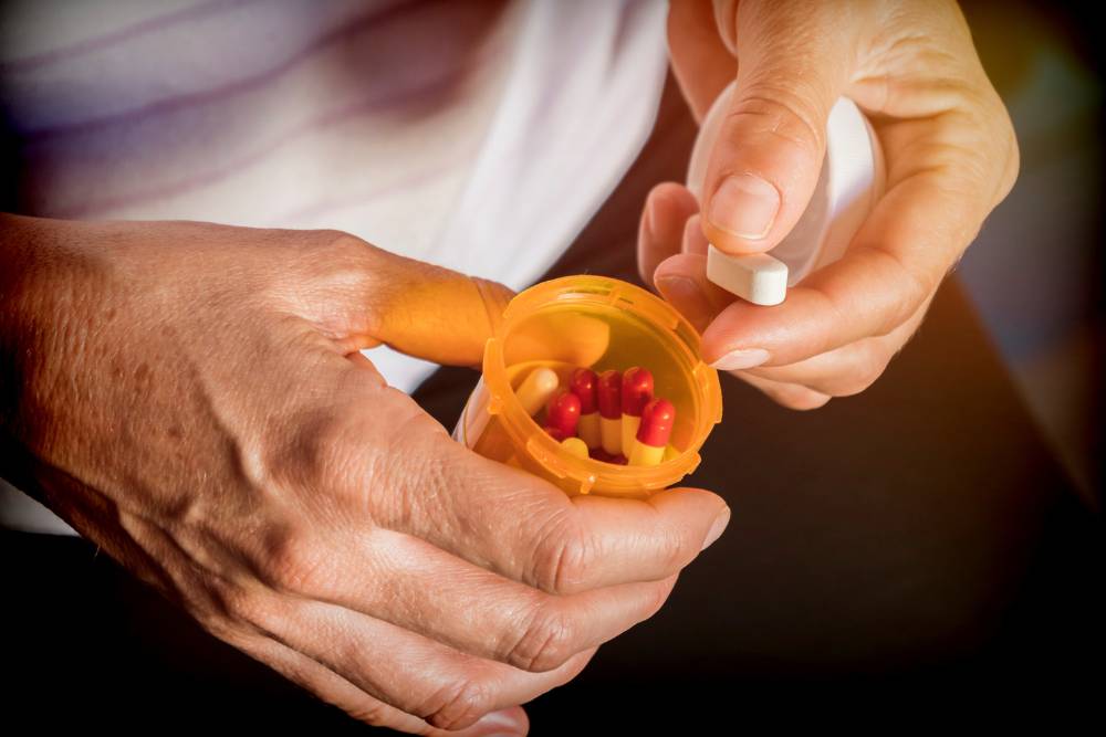 Close-up of hands holding a pill bottle and tablet, representing the challenges addressed through Fentanyl Detox in Orange County.